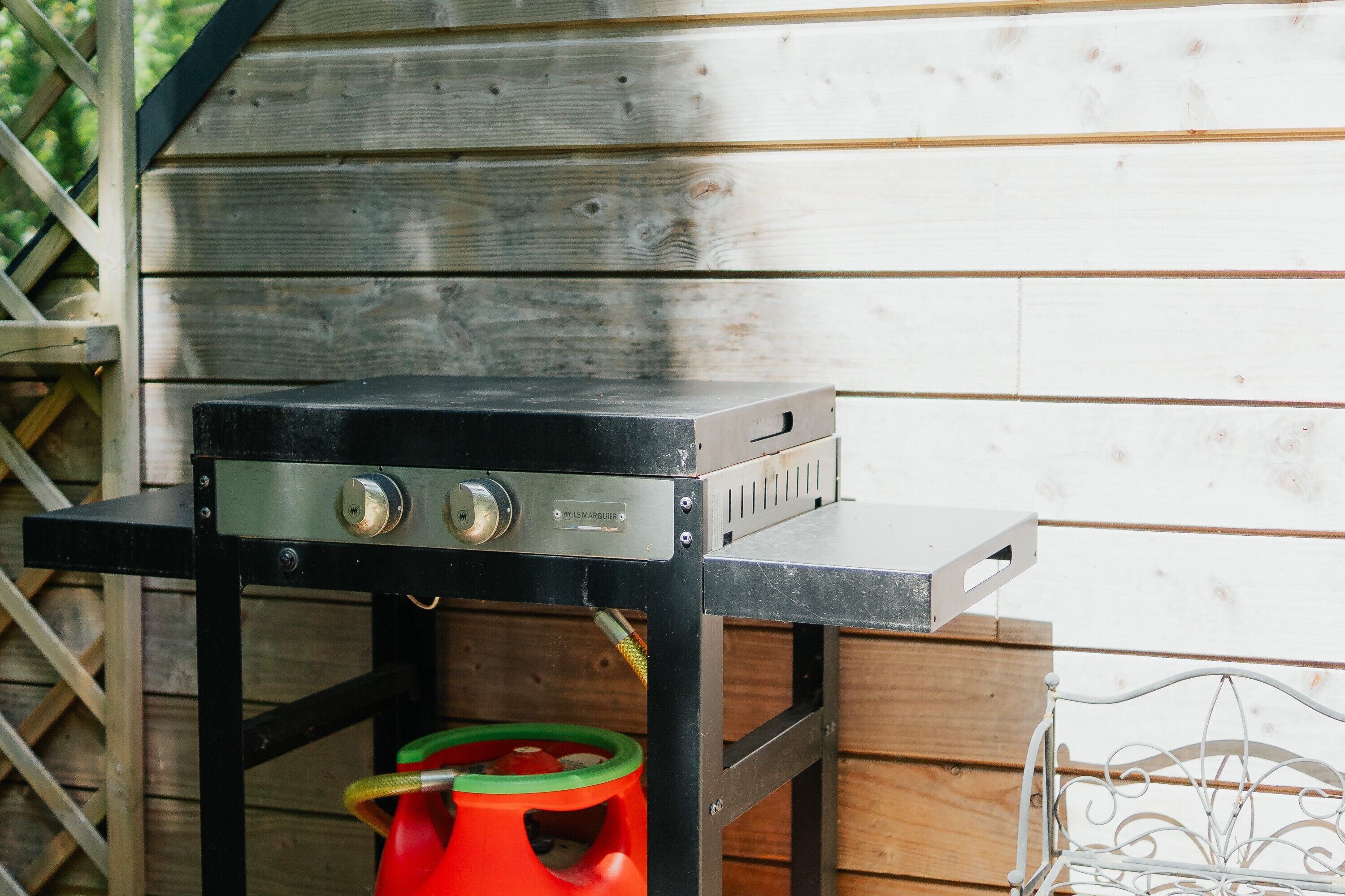 Un barbecue doté d’une structure métallique et de boutons de réglage, placé sous une structure en bois.