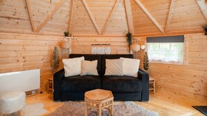 Ein Holzblockhaus-Interieur mit einem schwarzen Sofa, einem kleinen Holzschemel und einer weißen Heizkörper.