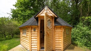 Eine Holzhütte mit geöffneter Tür, umgeben von viel Grün.