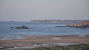 Eine Küstenlandschaft mit Sandstrand, Felsen und einem Leuchtturm in der Ferne.