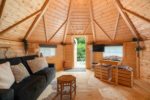 A cozy cabin interior with a wooden ceiling, a sofa, a dining table, and a view through a door. - Chalet 'Gite Petite Chaumière Kota Finland' with Private Terrace, Garden and Air Conditioning (Plurien)
