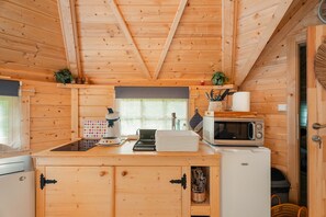 A wooden cabin interior with a kitchen area featuring a refrigerator, microwave, and a coffee maker. - Chalet 'Gite Petite Chaumière Kota Finland' with Private Terrace, Garden and Air Conditioning (Plurien)