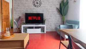 A living room with a brick wall, a clock, a TV, a sofa, a dining table, and a plant.