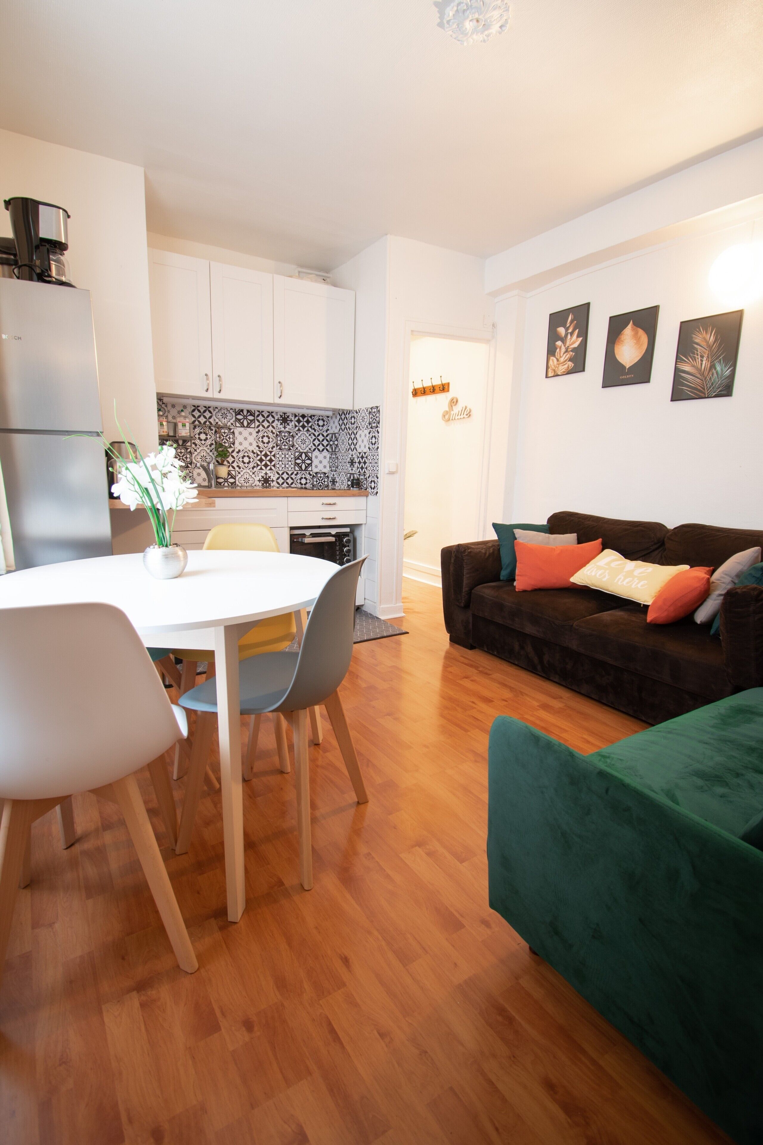 A modern living room with a dining area, a kitchen with patterned backsplash, and a green sofa with cushions.