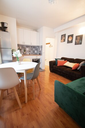 A modern living room with a dining area, a kitchen with patterned backsplash, and a green sofa with cushions.