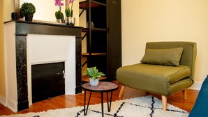 A living room with a fireplace, a green armchair, a round table with a plant, and a bookshelf. - Apartment 'Appartement 2 Pièces À Paris' with Wi-Fi (Gentilly)