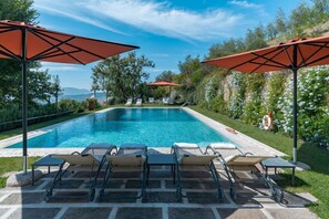 Une piscine entourée de verdure, avec des chaises longues et des parasols, et offrant une vue sur les montagnes.