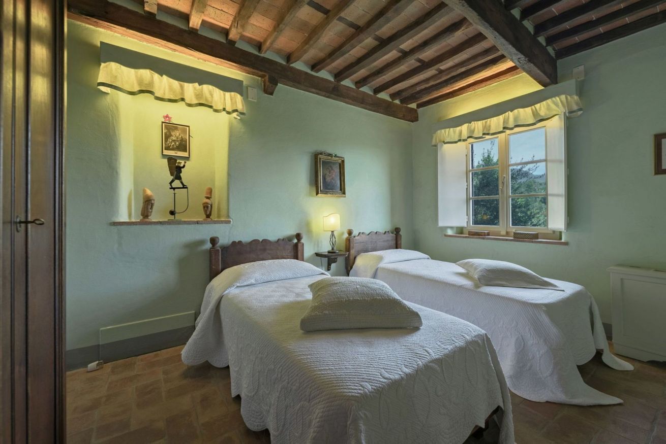 A bedroom with two beds, a wooden ceiling, a window with curtains, and a radiator.