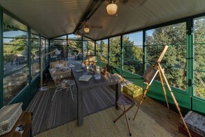 A room with a large table, chairs, a painting on easels, and a view through large windows.
