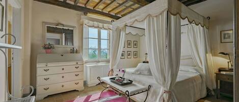 Une chambre à coucher avec un lit à baldaquin, une commode, une coiffeuse avec un miroir et une fenêtre avec des rideaux.