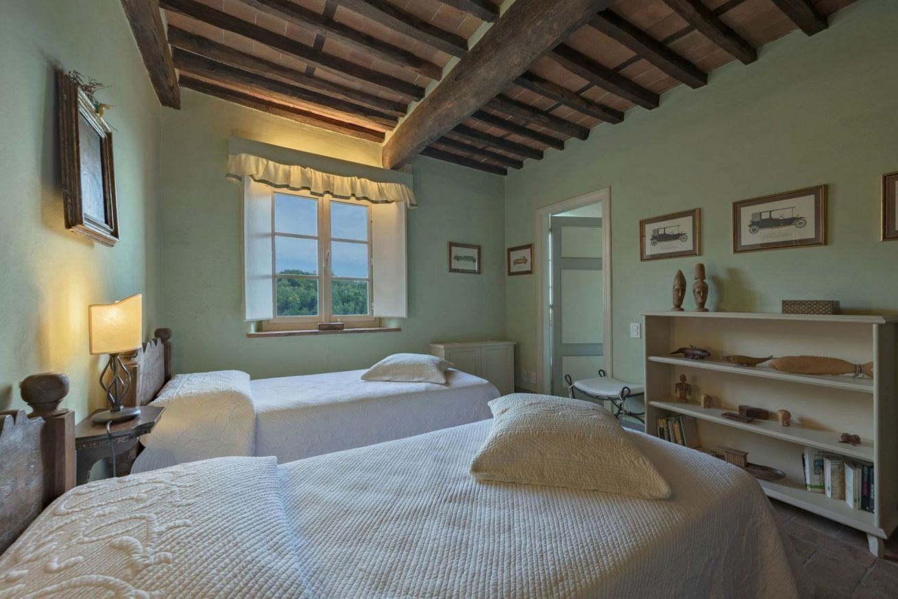 A room with two beds, a window with a view, a bookshelf, and a door.