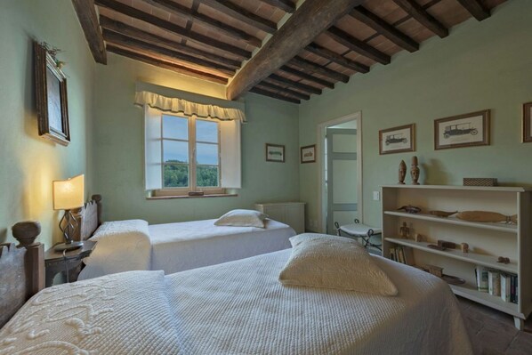 A room with two beds, a window with a view, a bookshelf, and a door.