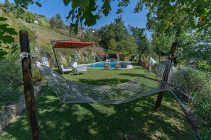 A hammock, a pool, and a grassy area with trees and a hill in the background.