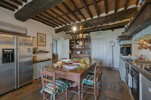 A rustic kitchen with a wooden table, chairs, a refrigerator, and a stove.