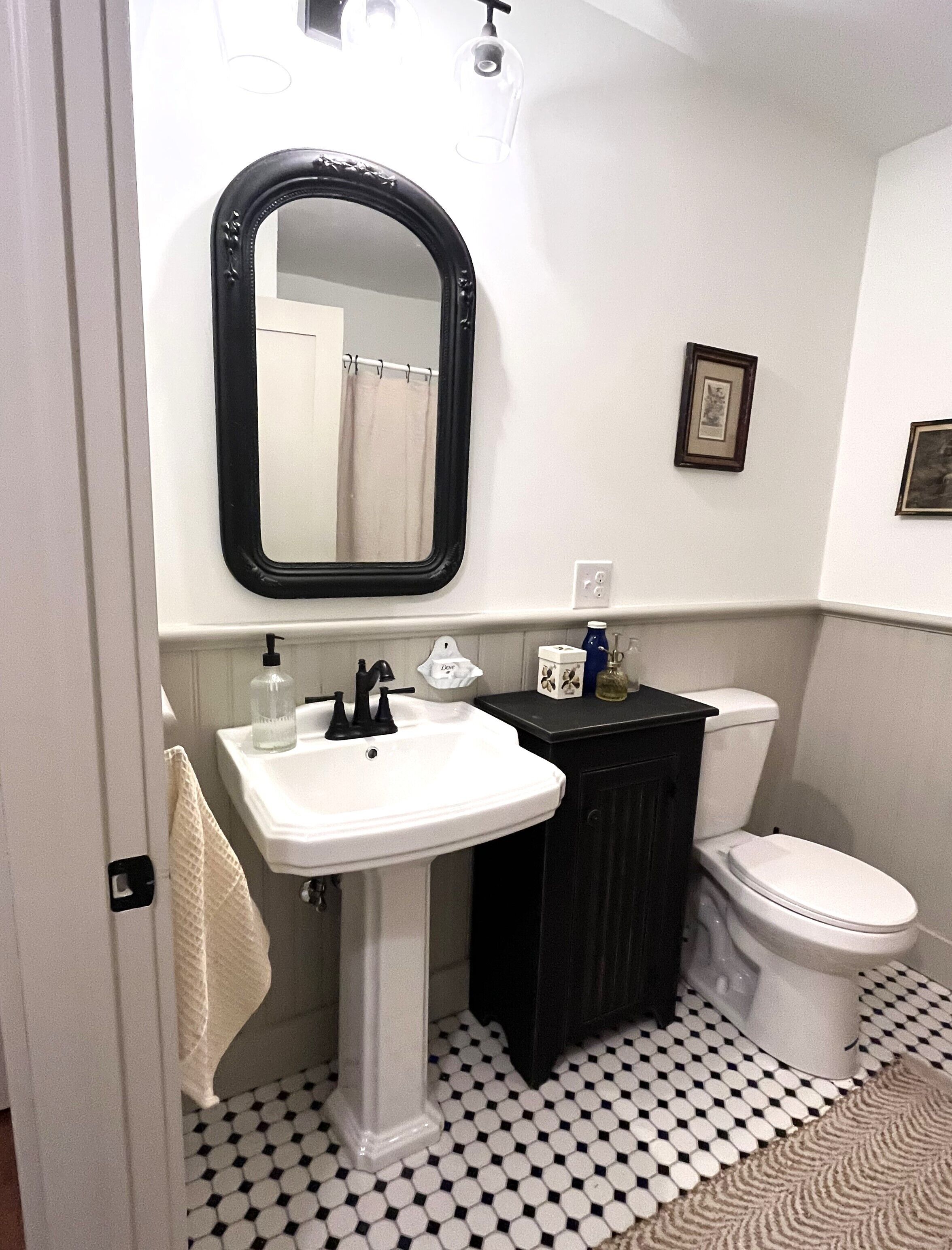 A bathroom with a white sink, black cabinet, and white toilet. There is a mirror above the sink and a framed picture on the wall.