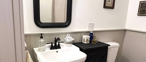 A bathroom with a white sink, black cabinet, and white toilet. There is a mirror above the sink and a framed picture on the wall.