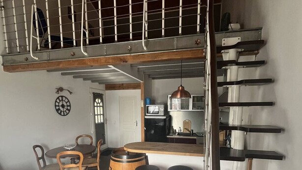 Een kleine keuken met een eethoek, een houten vat en een rode kruk.