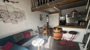 Een gezellige woonkamer met een bank, een salontafel en een eethoek met stoelen en een houten vat.