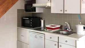 A compact kitchen with white cabinets, a microwave, a dishwasher, and a sink. - Charmante Maisonnette à Proximité Immédiate de la Plage (BISCARROSSE PLAGE)