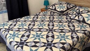 A bedroom with a geometric patterned bedspread, a wooden headboard, a nightstand with a lamp, and a wall-mounted picture. - Charmante Maisonnette à Proximité Immédiate de la Plage (BISCARROSSE PLAGE)