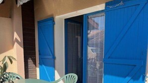 An outdoor patio with a table and chairs, a blue door, and a tiled floor. - Charmante Maisonnette à Proximité Immédiate de la Plage (BISCARROSSE PLAGE)