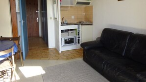 Un espacio habitable compacto con kitchenette, comedor y sofá de cuero negro.