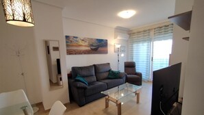 A living room with a sofa, a glass coffee table, a TV, and a painting on the wall.