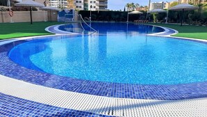 A circular swimming pool with a blue tiled edge, surrounded by a green lawn and palm trees.