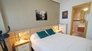 A hotel room with a bed, nightstands, a desk with a lamp, a bicycle, and a bathroom visible through an open door.