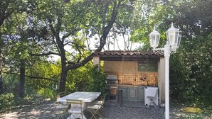 An outdoor kitchen with a table and chairs, surrounded by trees.