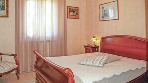 A bedroom with a wooden bed, a chair, a nightstand with a lamp, and two framed pictures on the wall.