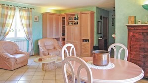 A living room with a pink dining table, two chairs, a leather sofa, a wooden cabinet, and a window with curtains.