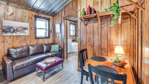 Un interior rústico de madera con un sofá de cuero, una mesa de comedor con sillas y una planta colgante.