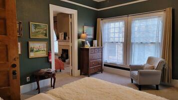 Un dormitorio con cama, una silla, cómoda, espejo y ventana con cortinas.