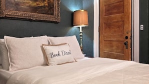 A bedroom with a bed, a painting, a lamp, and a wooden door. - The Kings Throne Inn and Guest House (Toledo)