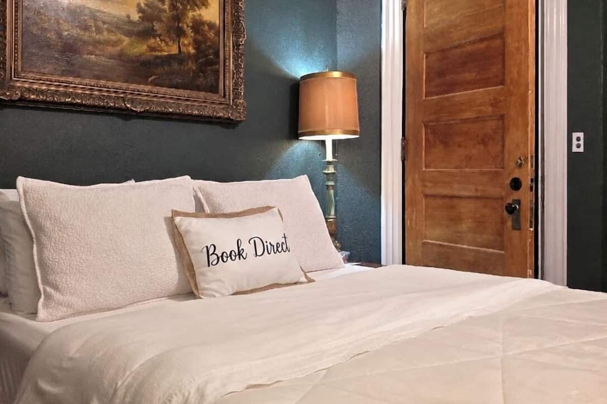 Ein Schlafzimmer mit einem Bett, einem Gemälde, einer Lampe und einer Holztür.