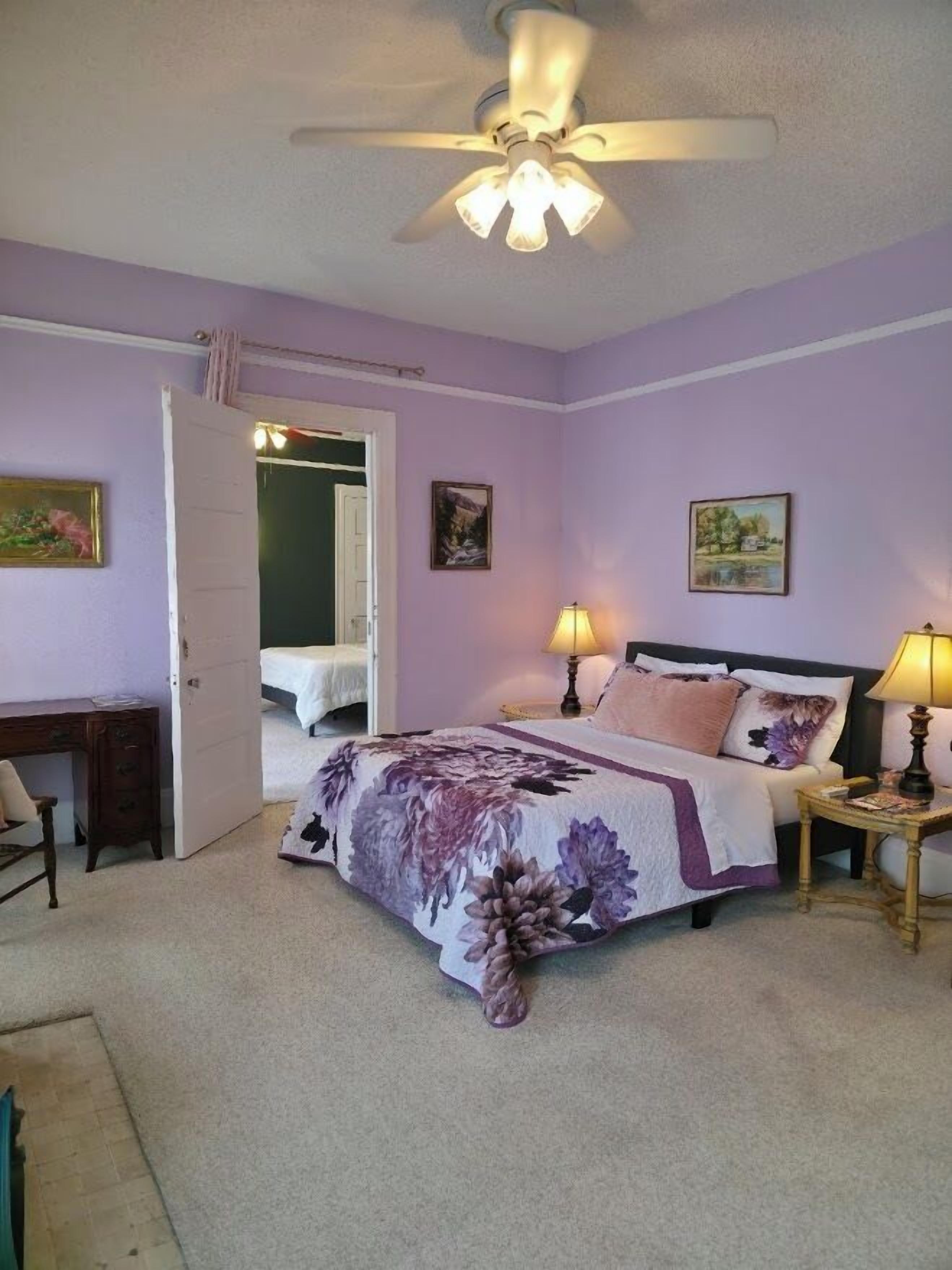A bedroom with a bed, two bedside tables, a desk, and a ceiling fan.