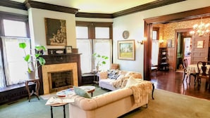 A living room with a fireplace, a sofa, a coffee table, and a dining area with chairs and a table. - The Kings Throne Inn and Guest House (Toledo)