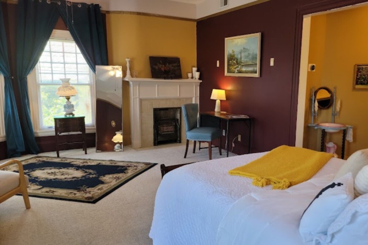 A hotel room with a bed, a fireplace, a desk, and a chair.