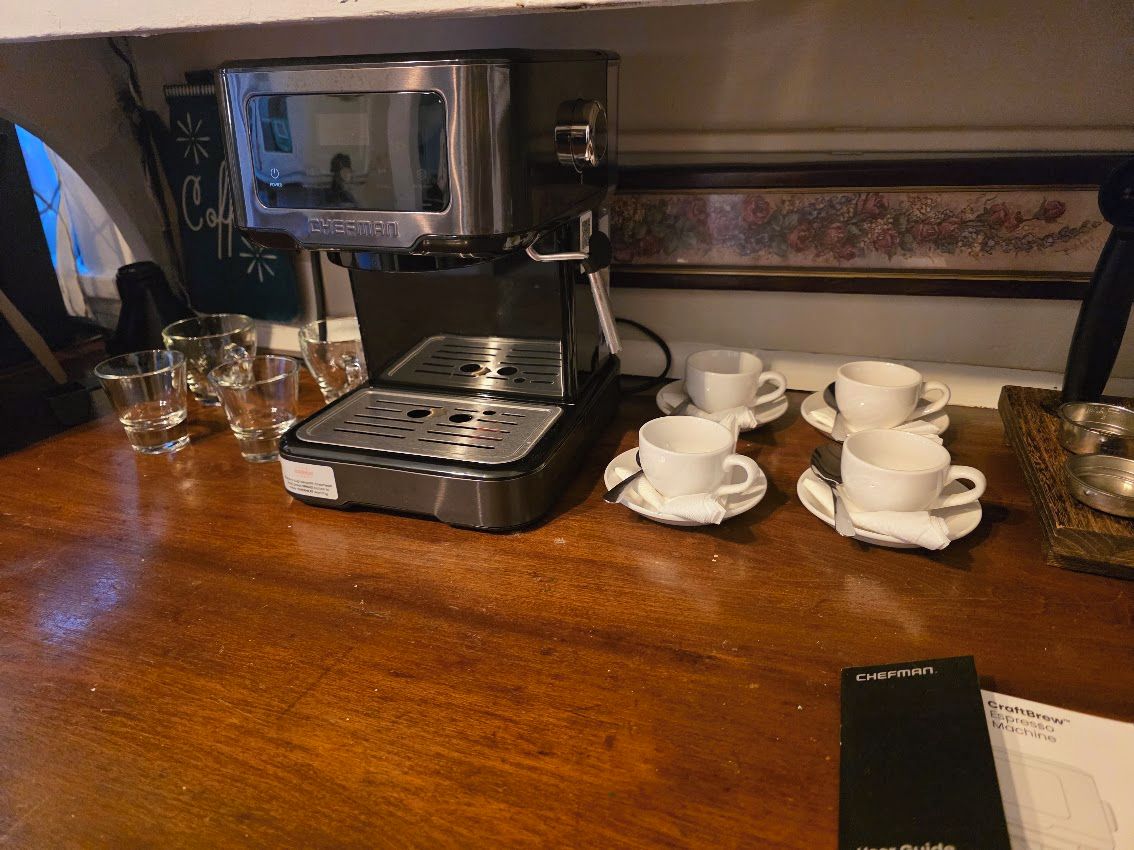 Une machine à café avec une cafetière, des tasses et des verres sur une table en bois.