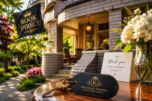 Ein Schild mit der Aufschrift 'BOOK DIRECT', eine Dankeskarte für die Direktbuchung, Schlüssel und ein Schild mit 'THE KINGS THRONE INN & GUEST HOUSE'.