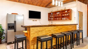 A kitchen with a wooden bar and stools, a refrigerator, and a TV mounted on the wall. - New Spacious Warren Dunes Beach & Winery Retreat w/Hot Tub & Pool Table (Bridgman)
