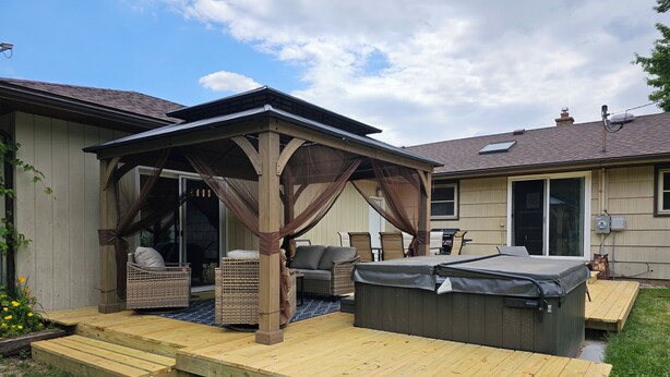 A covered patio area with outdoor furniture, a hot tub, and a wooden deck. - New Spacious Warren Dunes Beach & Winery Retreat w/Hot Tub & Pool Table (Bridgman)
