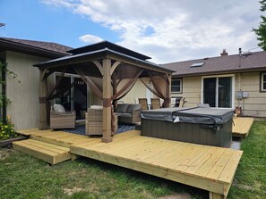 A covered patio area with outdoor furniture, a hot tub, and a wooden deck. - New Spacious Warren Dunes Beach & Winery Retreat w/Hot Tub & Pool Table (Bridgman)