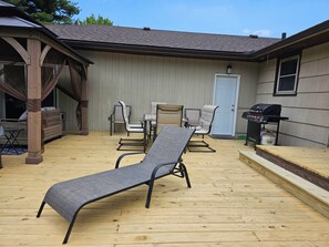 A covered patio area with a wooden deck, a grill, and outdoor furniture including a lounge chair and dining set.