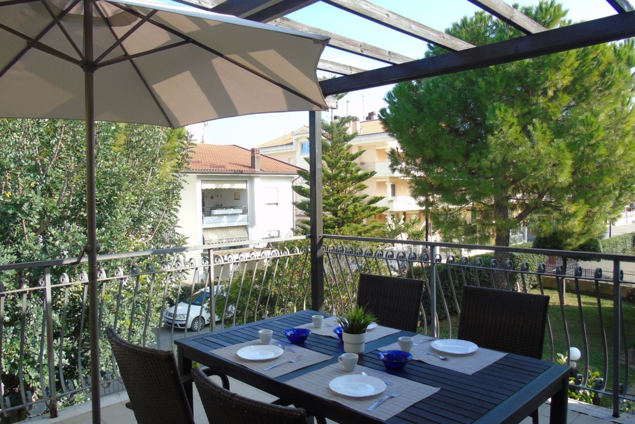 An outdoor dining area with a table set for two, surrounded by metal railings and greenery.