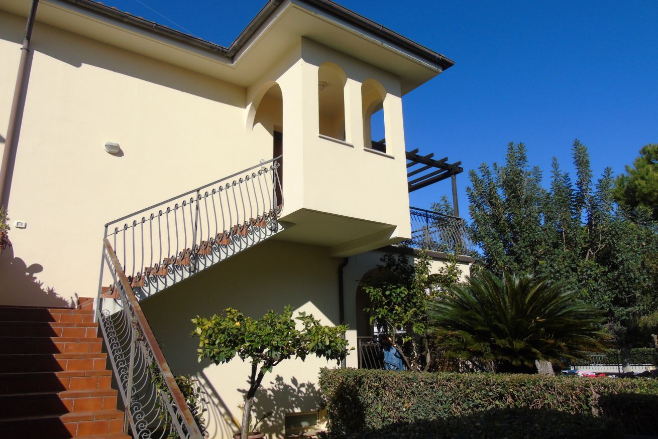 Un edificio con un balcone, una scala e un giardino alberato.