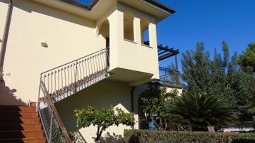 Un edificio con un balcone, una scala e un giardino alberato.