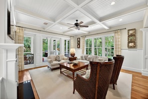 A spacious living room with a ceiling fan, large windows, and a fireplace. - Serene & Private Kiawah Retreat with Private Pool (Kiawah Island)