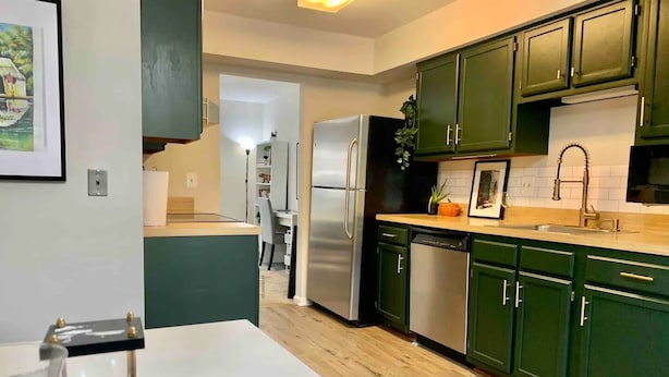Une cuisine moderne avec des meubles de couleur verte, des appareils électroménagers en acier inoxydable et un plan de travail blanc.